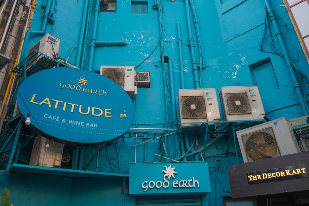 Fachada do café Good Earth Latitude 28 com placas de sinalização e unidades de ar-condicionado montadas na parede azul.